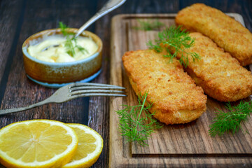 Close up of   Crispy breaded  deep fried fish fingers with breadcrumbs served  with remoulade sauce and  lemon Cod Fish Nuggets on rustic wood table background