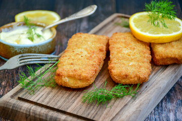 Close up of   Crispy breaded  deep fried fish fingers with breadcrumbs served  with remoulade sauce and  lemon Cod Fish Nuggets on rustic wood table background