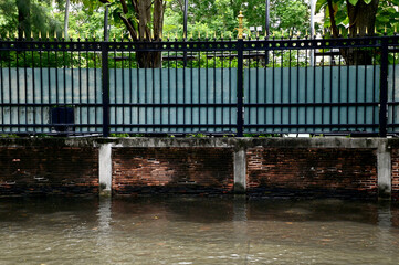 Flood water on the road beside an old brick wall with iron fence on the wall background in Thailand. Concept drive with caution.