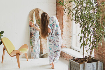 Fototapeta premium young woman with long hair combing her hair and applying makeup near the mirror