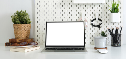 Front view computer laptop with blank screen, book, coffee cup and houseplants on white table.