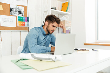 Fototapeta na wymiar Young white man working with laptop while sitting at desk in office