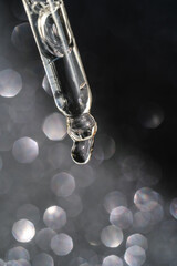 Cosmetic pipette with a drop on dark background.