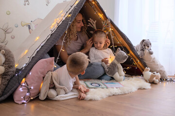 Mom with children in a hut reading a book, playing