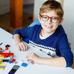 Little blond child with eye glasses playing with lots of colorful plastic blocks. Adorable school...