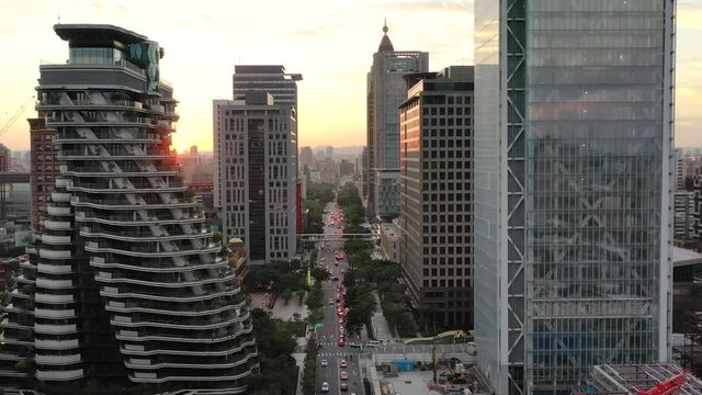 Cinematic aerial pull out shot, drone flying above Songgao road with high-rise skyscrapers and apartment complex alongside at sunset in downtown Xinyi district, Taipei city, Taiwan.
