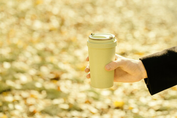 Reusable eco friendly bamboo cup with lid for take away coffee close up in hands on autumn blurred background with bokeh
