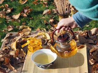 Senior woman is hand pours tea into a bowl with national traditional ornament.