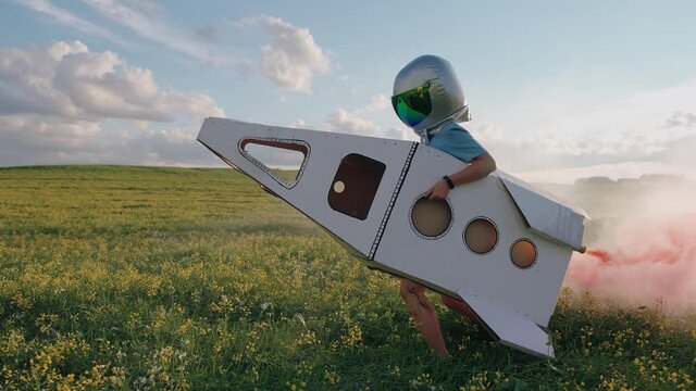 Countryside, boy plays in an astronaut helmet in nature with a cardboard model of a space shuttle, a boy runs through a field of rapeseed dreaming of flying into space, pink smoke, 4k slow motion.