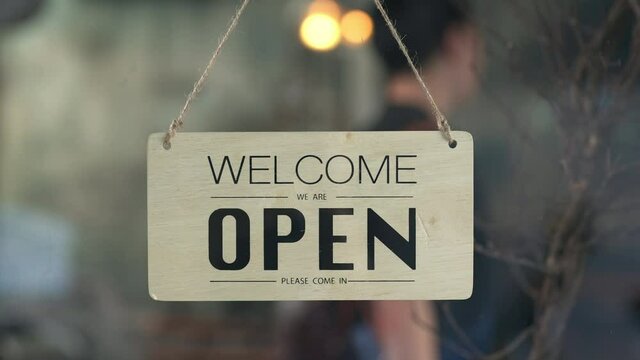 Asian man coffee shop barista walking to cafe door and turning hanging closed sign to open. Male waiter preparing restaurant service to customer. Small business owner and part time job working concept