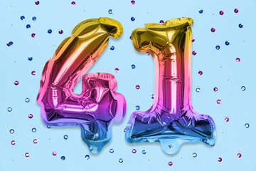 Rainbow foil balloon number, digit forty one on a blue background with sequins. Birthday greeting...
