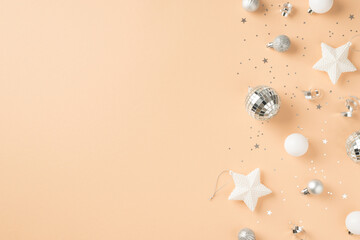 Top view photo of white and silver christmas tree decorations stars disco balls sequins and serpentine on isolated beige background with copyspace