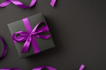 Above photo of black giftbox with purple ribbon wrapped as bow isolated on the black background