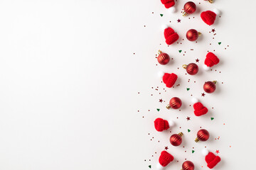 Top view photo of row composition red christmas tree decorations small balls bobble hats and multicolor confetti on isolated white background with empty space