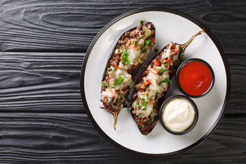 Delicious eggplant stuffed with ground beef, vegetables and baked with cheese, served with sauces close-up in a plate on the table. horizontal top view from above