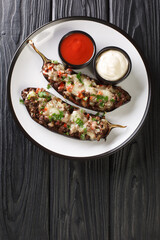 Baked eggplant stuffed with ground beef, vegetables and cheese, served with sauces close-up in a plate on the table. vertical top view from above
