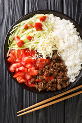 Takoraisu Okinawan Taco Rice with ground beef, vegetables, cheese and sauce close-up in a bowl on...