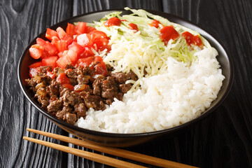 Japanese taco rice with ground beef, vegetables, cheese and sauce close-up in a bowl on the table. horizontal