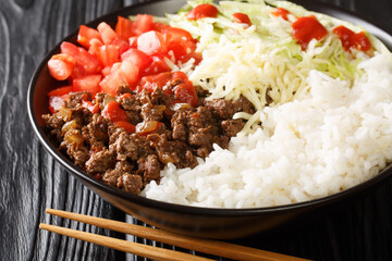 Taco rice takoraisu is a Mexican Japanese fusion dish consisting of seasoned ground beef, shredded lettuce, and chopped tomatoes served over a bed of white rice close-up in a bowl on the table