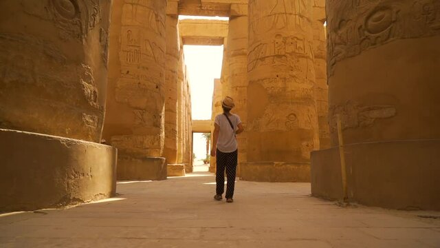 A young woman walking through the Karnak temple and its beautiful hieroglyphic columns, the great sanctuary of Amun. Egypt