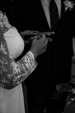 A bride in a white wedding dress puts on an engagement ring to a groom in a black suit at the wedding ceremony. Black and white wedding photo during quarantine. High quality photo