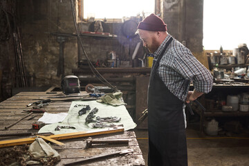 Manual worker in apron standing in front of his workplace with tools and starting to work in workshop