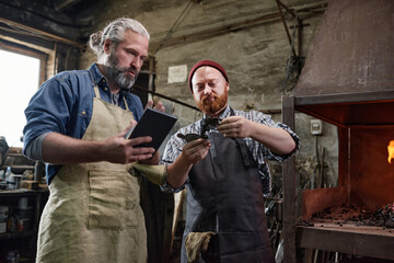 Man showing the metallic detail to his colleague while he using tablet pc they working in team in the factory