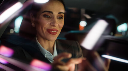 Fototapeta na wymiar Beautiful Businesswoman is Commuting from Office in a Backseat of Her Luxury Car at Night. Entrepreneur Passenger Traveling in a Transfer Taxi in Urban City Street with Working Neon Signs.