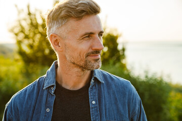 Grey man smiling and looking aside while standing outdoors