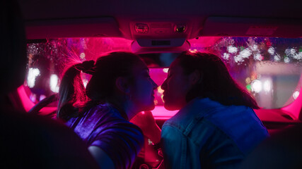 Romantic Young Adult Lesbian Female Couple Kiss on the Front Seat of Their Car on a Rainy Night in the City. Women in Love on a Date in Neon Urban Environment. Concept of LGBT, Relations and Driving.