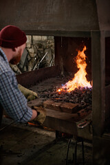 Rear view of manual worker putting coal into furnace in the workshop