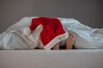 Children's feet on the bed in a Santa hat. home New Year and Christmas. Happy Holidays. space for...