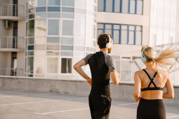 Obraz premium Young man and woman in headphones running together on parking