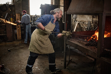 Craftsman adding coal in furnace in the blacksmith shop