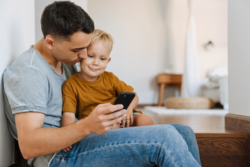 Obraz premium Young father and son using mobile phone while sitting on stairs