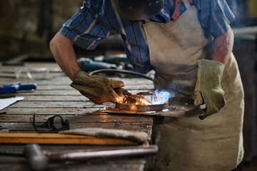 Close-up of smith in gloves making details from iron at his workplace in workshop
