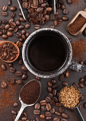 Coffee cup with various scoops of ground and bean coffee and freeze dried instant coffee granules on brown background.