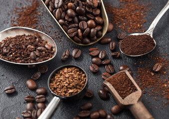 Bean and ground coffee and freeze dried instant coffee granules in various spoons and scoops on black background.