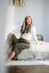 Mature asian woman with grey hair sitting on bed