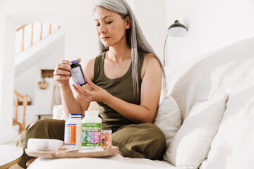 Mature asian woman taking her medication while sitting on couch