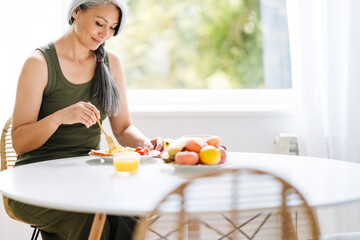 Mature asian woman with grey hair having breakfast at home