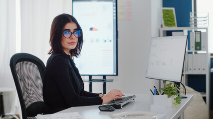Portrait of engineer using computer for charts design at desk. Businesswoman looking at camera and working with monitor for project planning. Person with corporate job at company office