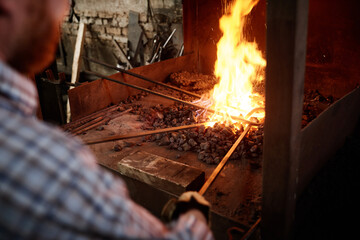 Close-up of blacksmiths holding metallic sticks and heating them with fire in the furnace