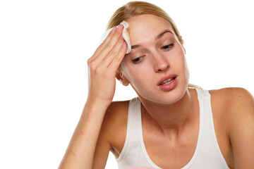 young blond woman with cleans her face with cotton pad