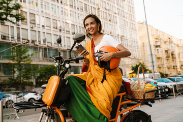 Young indian woman wearing sari using cellphone while sitting on scooter
