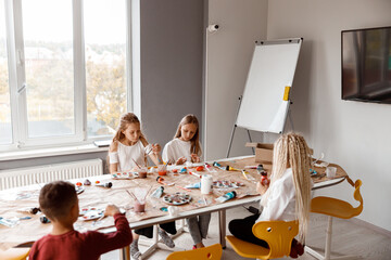 Children sitting at the table and enthusiastically drawing with watercolors on paper