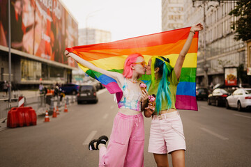 Young lesbian couple kissing while walking with rainbow flag