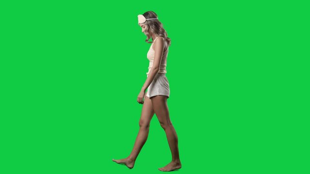 Side view of calm young woman in pajamas walking and looking down. Full body isolated on green screen background