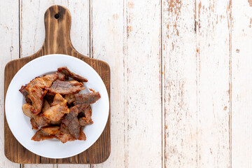 tasty fried pork in simply ceramic plate on an old wooden cutting board over the white wood texture background with copy space for text, top table view, flat lay