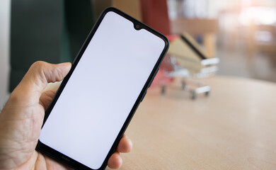 Close up, human hand holding mobile phone and blur supermarket cart, credit card and shopping bags on background